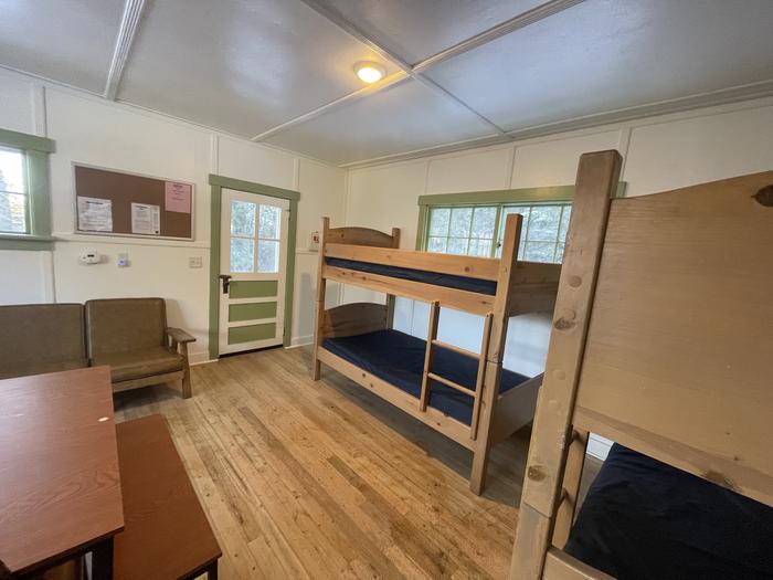 Living room with bunk bedsThe living room has a wooden couch with cushions and two bunk beds.