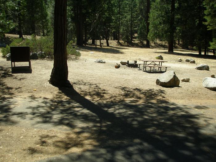 Scene of campsite with parking pad, bear box, picnic table, fire ring, and in the background a tent pad. Parking pad, bear box, picnic table, and fire ring,