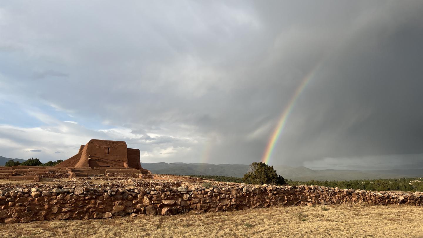 Pecos Mission Church remains with dark sky and rainbow in background. 