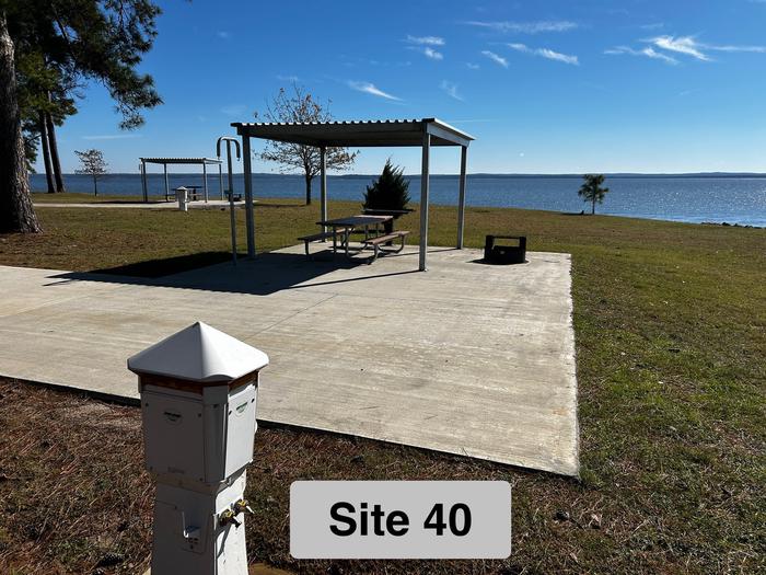 A photo of Site 40 of Loop LOOB at RAYBURN with Picnic Table, Electricity Hookup, Fire Pit, Shade, Waterfront, Lantern Pole, Water Hookup, Lean To / ShelterView of site 40 with Power Pedestal in the foreground, Parking Pad, Shelter with Picnic Table, Grill Stand, Lantern Pole, Fire Ring with Grill Rack. The view over the Lake to the Northeast. 