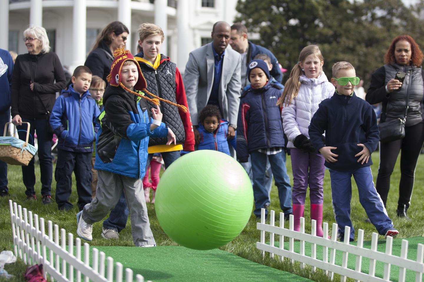 Child play a ball rolling game with people observing the game in the background at the white house easter egg rollA child rolls a ball at the White House Easter Roll 