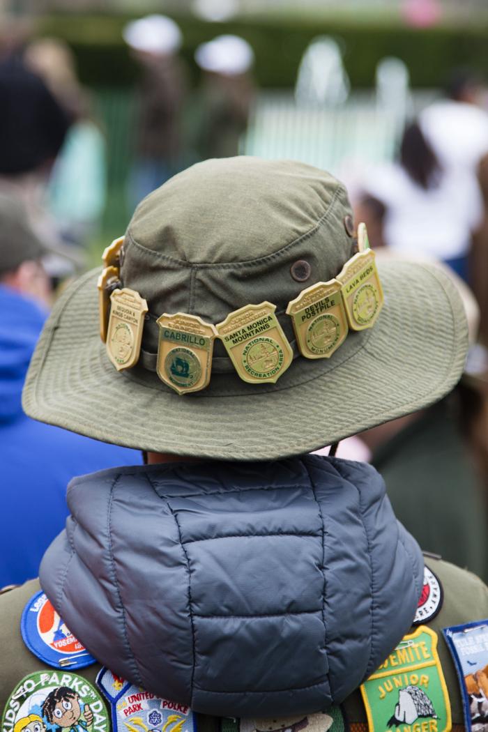 A person standing with their face turned away from the camera wearing a bucket hat adorned with Forest Service MedalsA visitor at the White House Easter Egg Roll observing the festivities adorned with Forest Service badges and a mix of other patches. 