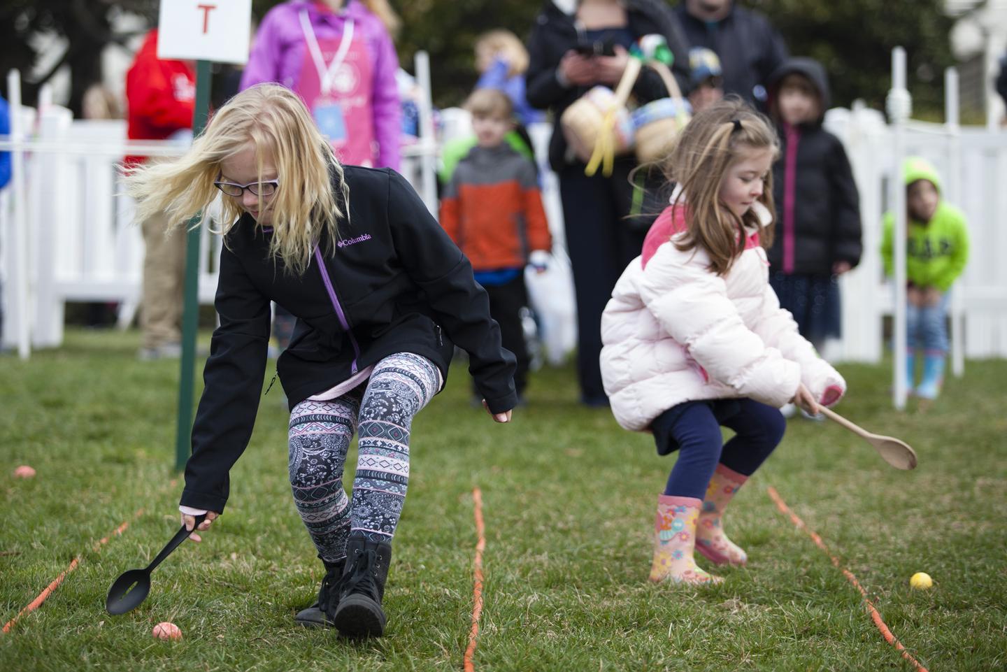 Two children rolling eggs with spoons at the White House Easter Egg Roll 