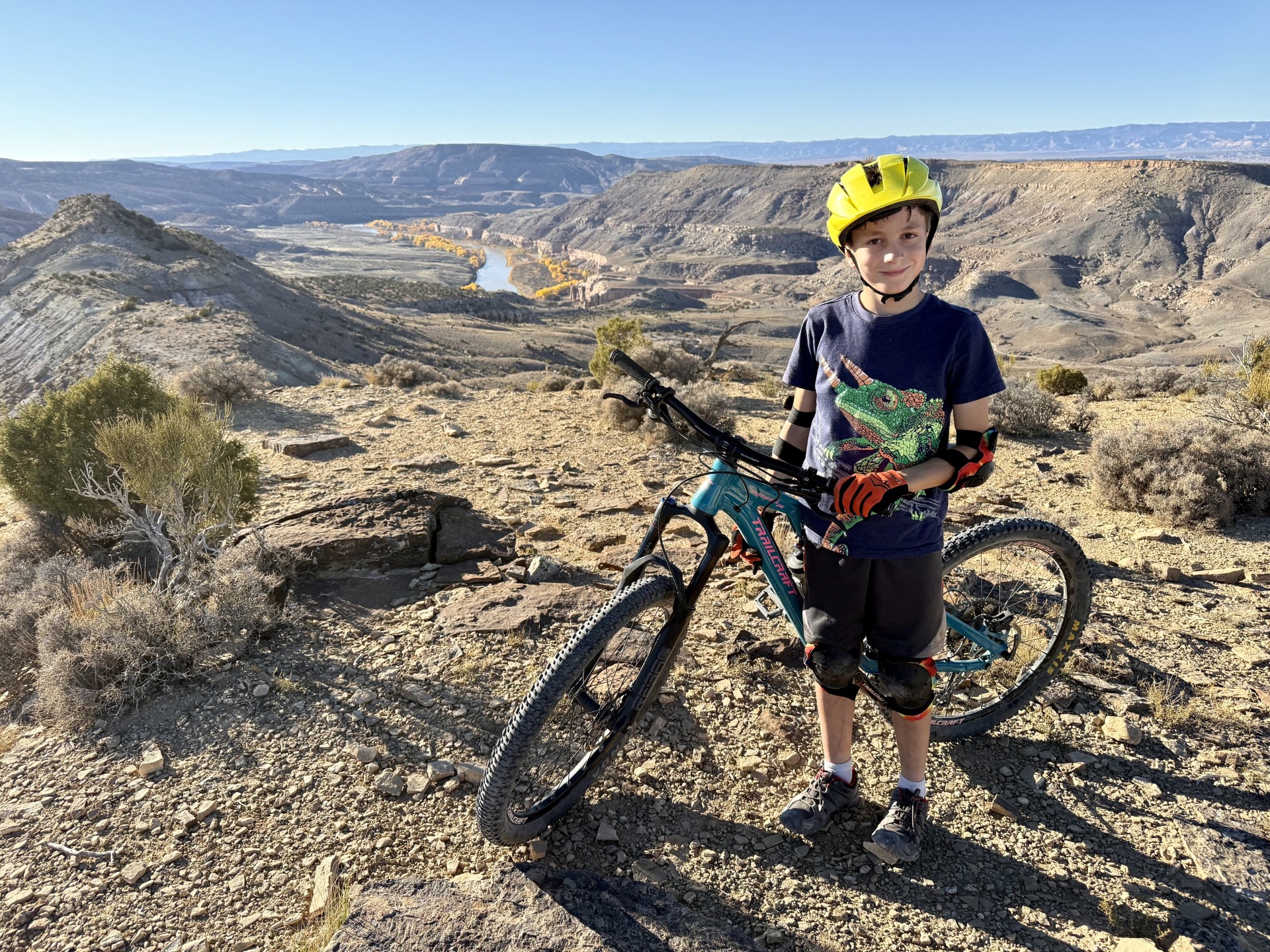 Kid with bike and helmet in desert landscape with river behind