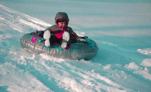 child tubing down a snow hill