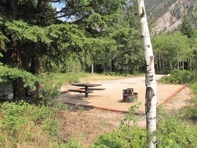 Campsite with trees, picnic table, fire pit, mountain in backgroundPhoto of campsite with fire pit and picnic table