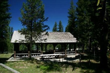 Large, covered picnic pavilion near an open meadow in a pine forest under deep blue sky.SOUTH SHORE PAVILION