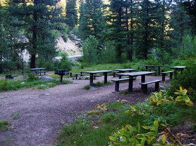 A group of picnic tables with benches near a raised grill.Hayfork features plentiful equipment to grill and dine as a group.