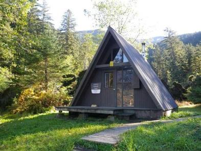 A-frame Garnet Ledge Cabin with wooden walkway and trees with grass in frontGarnet Ledge Cabin