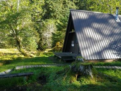 A frame cabin from the side with porch and trees surrounding itGarnet Ledge Cabin