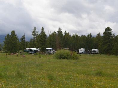 Trucks and trailers in a group campground with a grassy meadow and pines in the background.Browne Lake Campground