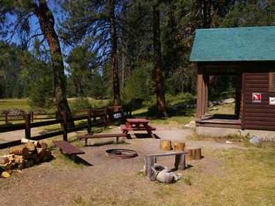 A picnic table, benches, and a fire ring next to a rustic cabin.Deer Park Cabin's outdoor campfire area.