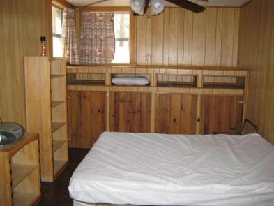 Horsethief Cabin bedroom with full bed, bookcases at the foot, two windows, ceiling fan and cabinets on back wall.bedroom