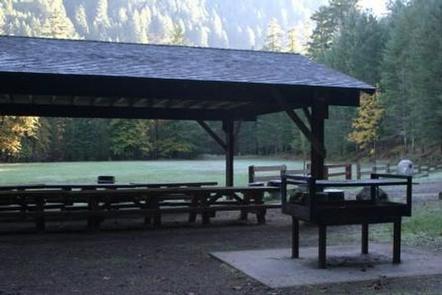 Group picnic shelter and barbecue next to large flat lawn ringed by mostly conifer forest.STEAMBOAT BALL FIELD GROUP SITE