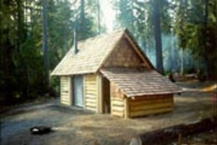 Fire ring in front of log cabin with attached, covered wood shed  in misty conifer forest.Timpanogas cabin.