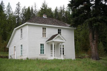 White, two-story house on a grassy hill next to a fir forest.CARETAKERS CABIN
