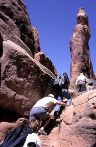 A line of people ascending a steep sandstone face.During these physically demanding hikes, you will walk and climb on irregular and broken sandstone, along narrow ledges above drop-offs, and in loose sand.