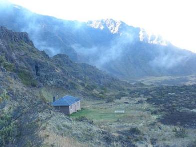 view from above of cabin against a sloping cliff, fog drifting in the backgroundHōlua Cabin
