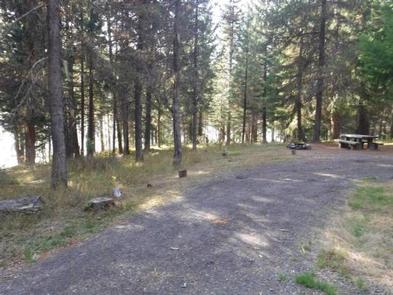 Flat gravel driveway leading to campsite with picnic table and fire ring in pine forest.BUNKER HILL CAMPGROUND